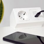 Eine Steckdose mit integriertem WLAN-Stromzähler, die an ein Balkonkraftwerk angeschlossen ist und die Energieerzeugung auf einem Smartphone-Display anzeigt.