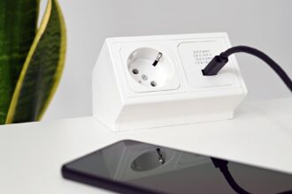 Eine Steckdose mit integriertem WLAN-Stromzähler, die an ein Balkonkraftwerk angeschlossen ist und die Energieerzeugung auf einem Smartphone-Display anzeigt.