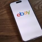 Ein Smartphone zeigt eine App zur Steuerung von smarten Heizkörperthermostaten, daneben liegen einige ungeöffnete Geräte in eBay-Umverpackungen.