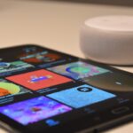 Kompakter Amazon Echo Dot in weiß auf einem Holztisch, umgeben von smarten Geräten wie einer Lampe und einem Thermostat.