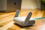 Ein einzelner TP-Link Deco BE65 WLAN-Router in Weiß, modernes, schlankes Design, steht auf einem Holztisch in einem hellen, gemütlichen Wohnzimmer, umgeben von dezenten Smart-Home-Geräten, symbolisiert schnelles, stabiles Wi-Fi 7 für das ganze Zuhause.
