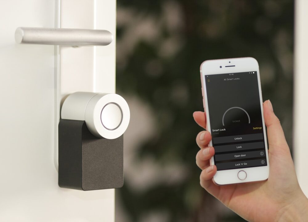 Ein schlankes, weißes Nuki Keypad mit beleuchtetem Zahlenfeld ist neben einer modernen, smarten Haustür montiert. Eine Hand tippt eine PIN ein, während die Tür leicht geöffnet ist – ein Symbol für komfortablen, schlüssellosen Zutritt im smarten Zuhause.